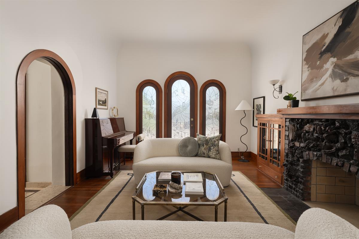 Living room with three arched windows, a lava rock fireplace, built-in wood cabinets and a piano