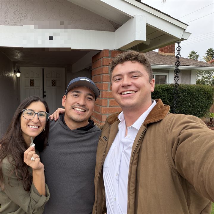 Jared Harman with two clients outside their new home, one holding up the keys
