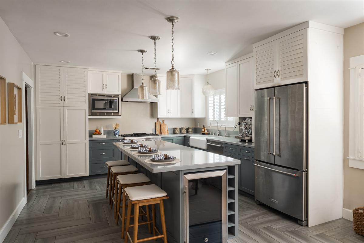 Kitchen with white upper cabinets, gray lower cabinets, a stainless range and an island with four stools
