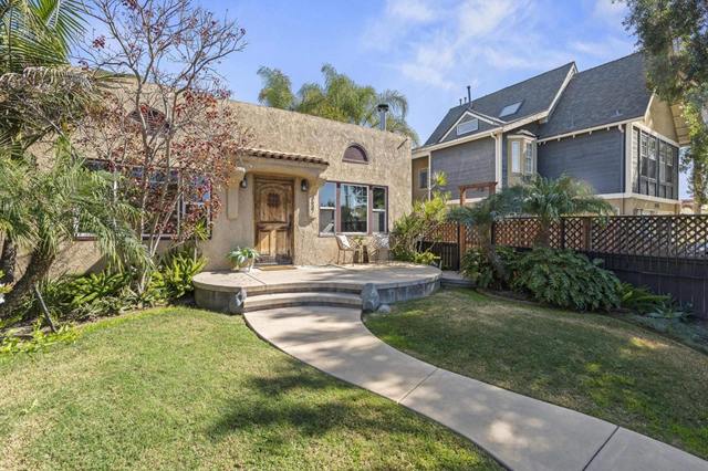 Stucco bungalow with an arched front door, a curved walkway, palms and a lawn